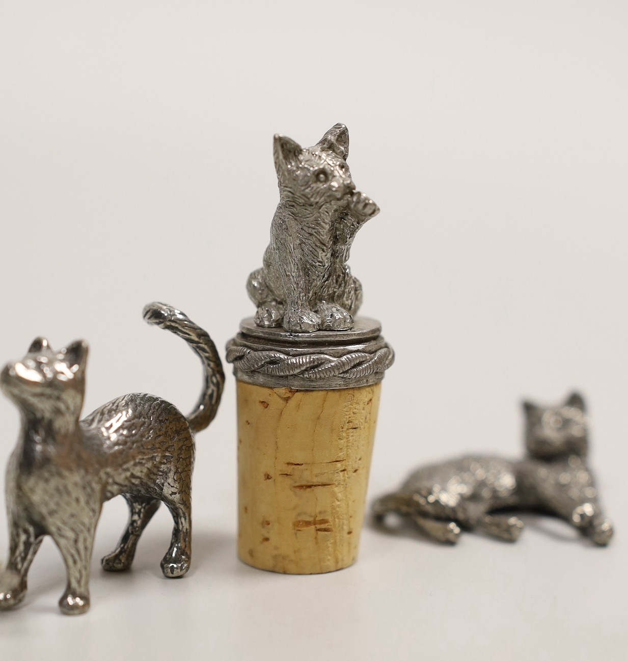 A modern silver miniature free standing model of a cat, with raised paw, London, 1995, length 37mm, together with four other base metal cats and a mouse and a cork stopper with cat finial.